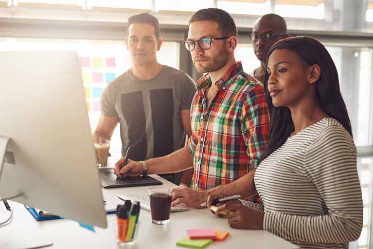 Group of four entrepreneurs wearing casual clothing while standing around computer